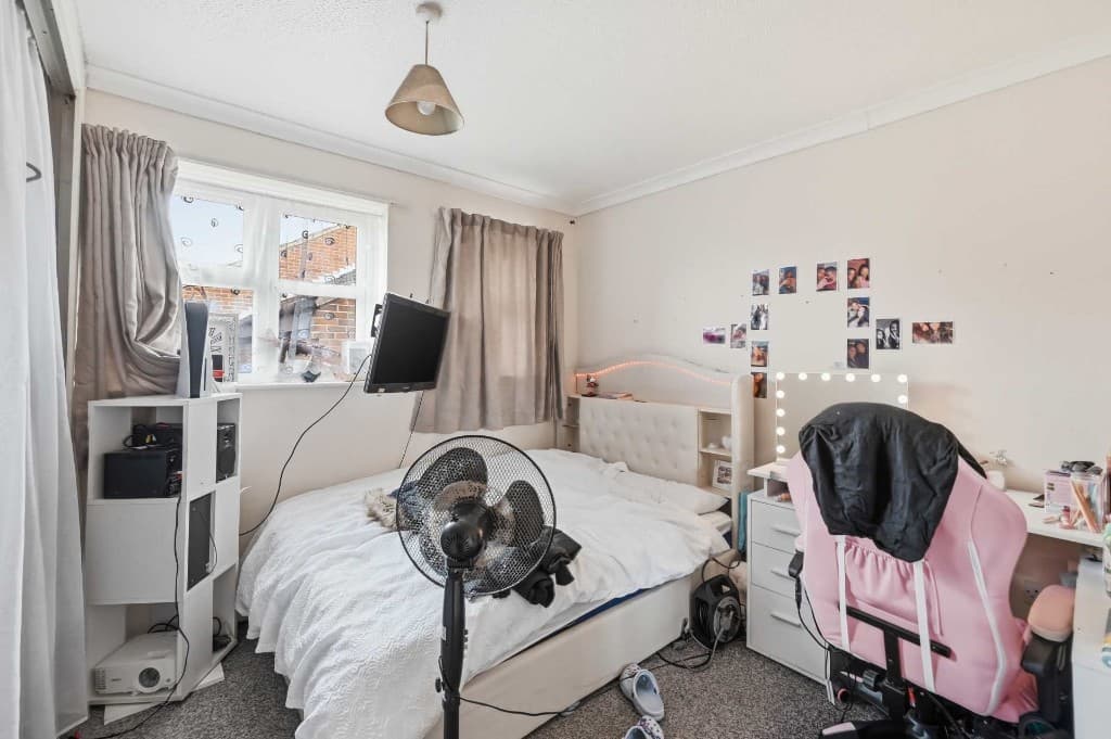 Bedroom cluttered with a fan, cables, electronics and belongings before cleanup
