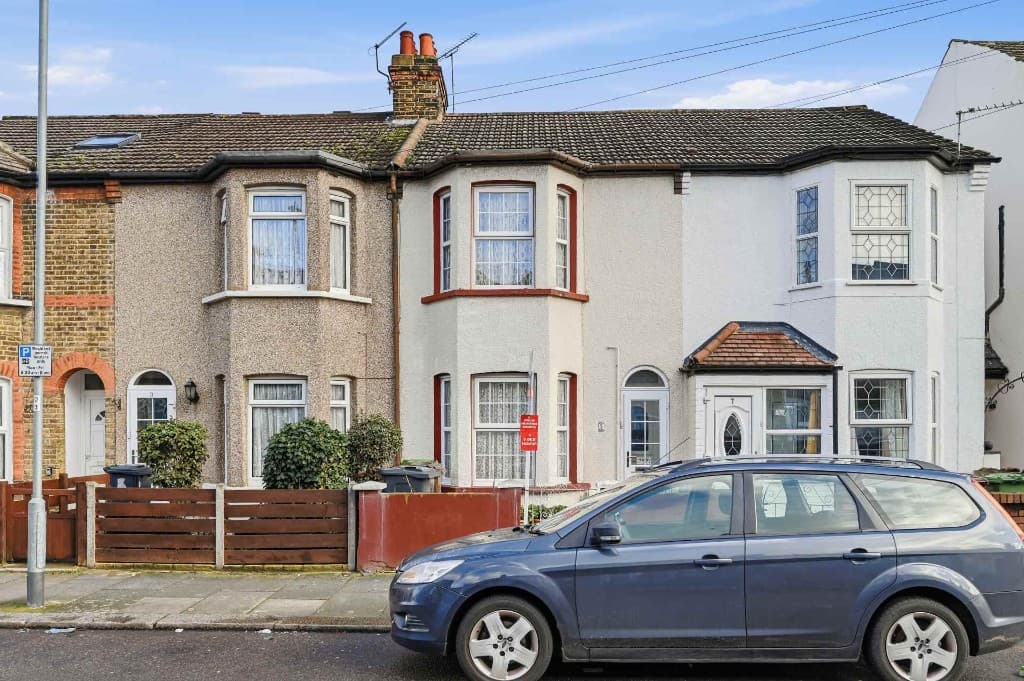 Terraced house with a car parked outside, bins and a for-sale board before cleanup