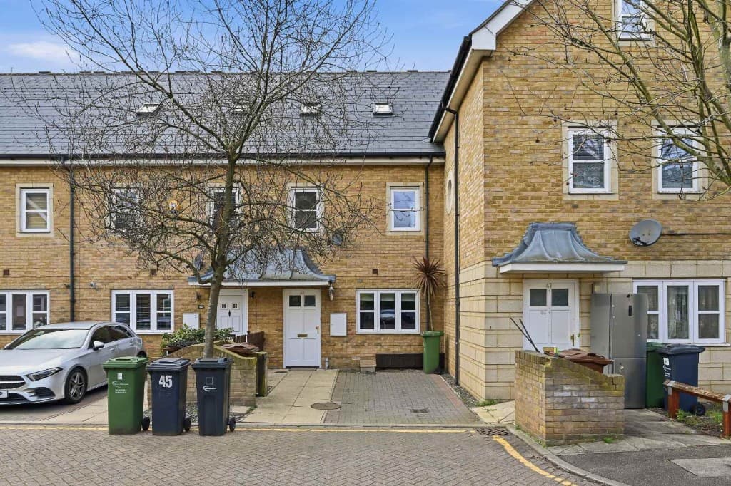 Townhouse exterior with wheelie bins, a parked car and an old fridge before cleanup